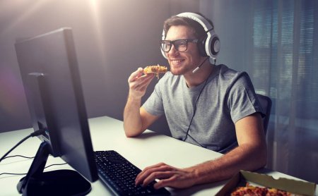 gamer with headphones eating pizza in front of computer screen